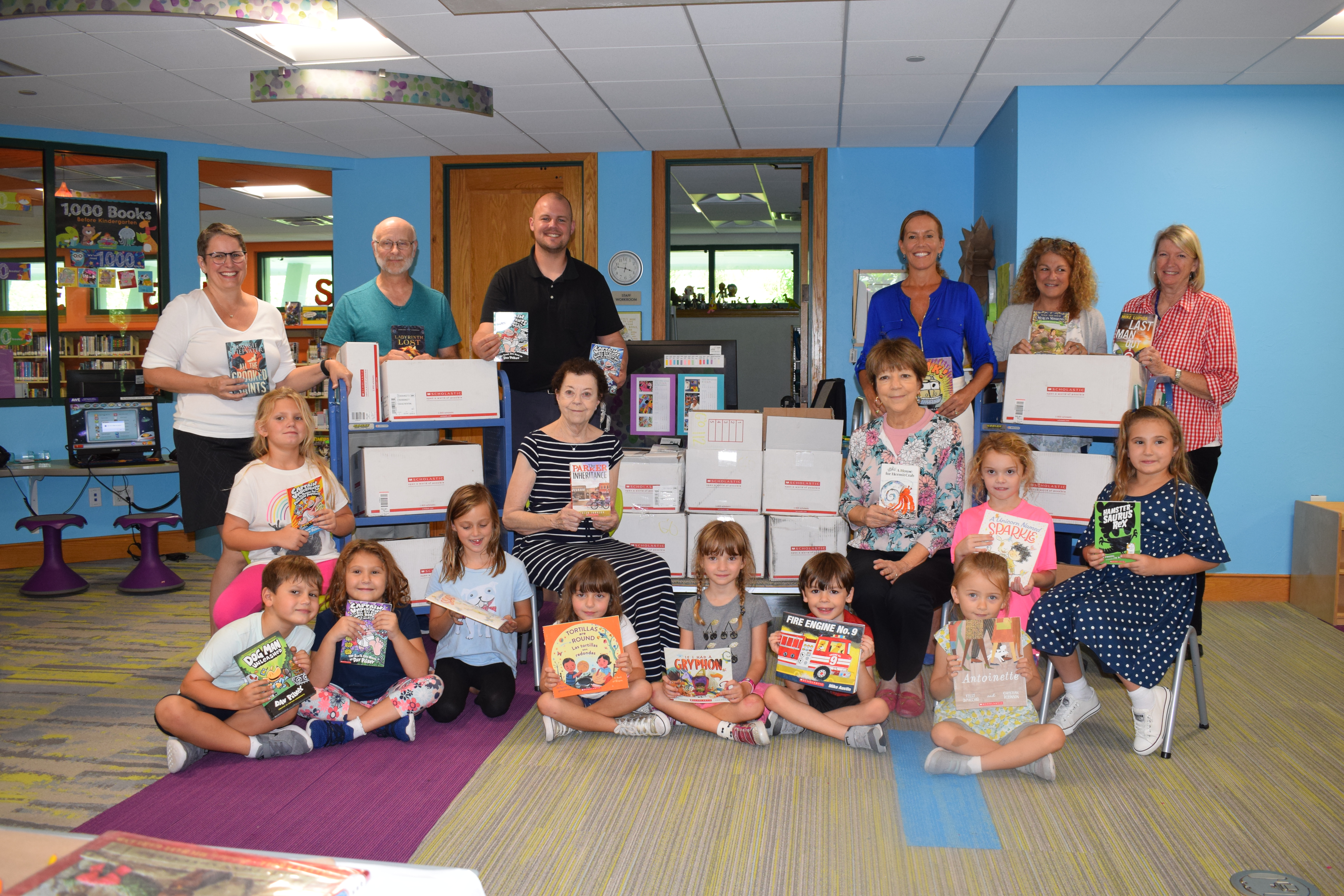 Group of children and adults holding books, surrounded with boxes of books