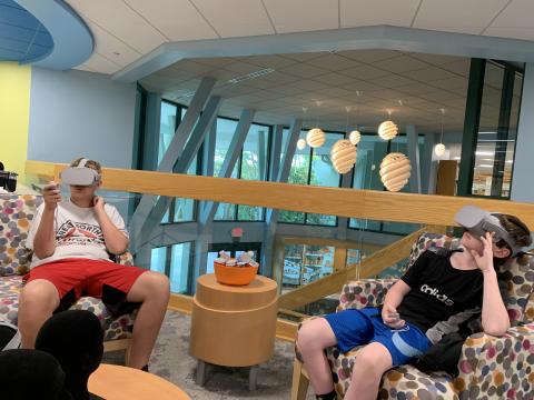 Two teens, seated, wearing virtual reality headsets
