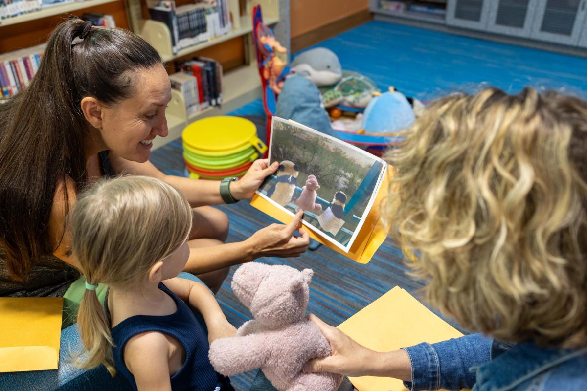patrons looking at a photo of the adventures their stuffed buddy went on overnight in the library